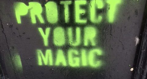 Neon green words saying “Protect Your Magic” painted on a black background