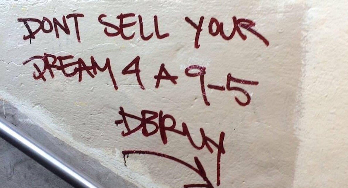 Graffiti on a wall that reads “Don’t Sell Your Dream for a 9-5”