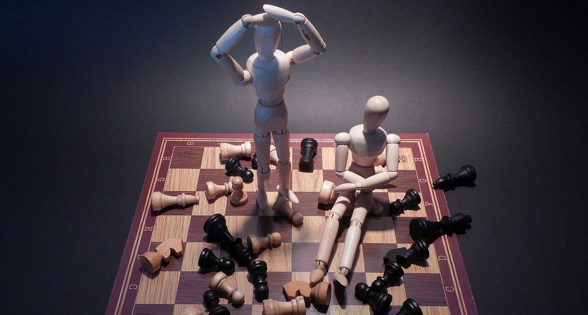Wooden figures on a chess board with chess pieces knocked down around them