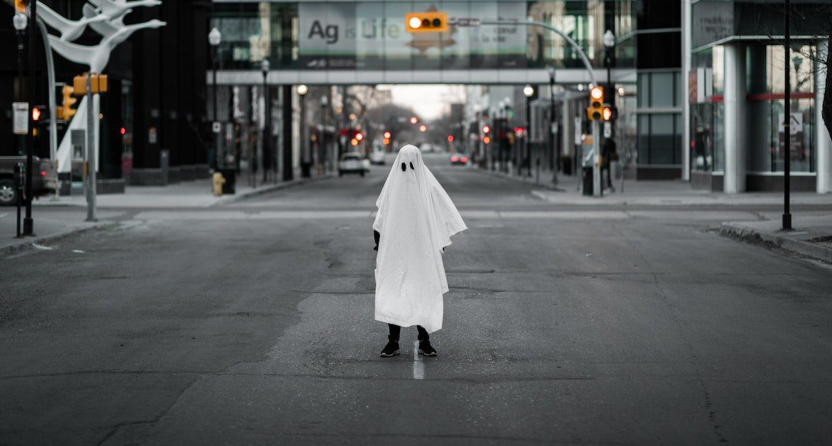 Person standing in the street covered in a white sheet resembling a ghost costume