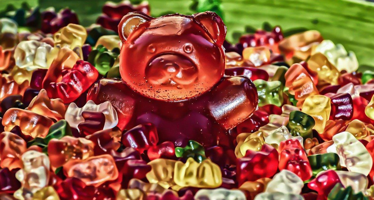 A giant, red gummy bear candy surrounded by normal-sized gummy bears